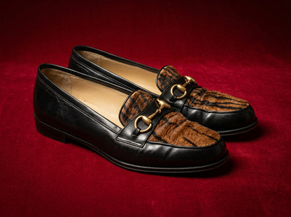 Gucci horsebit loafers with tiger calf-hair on red editorial backdrop, three-quarter view